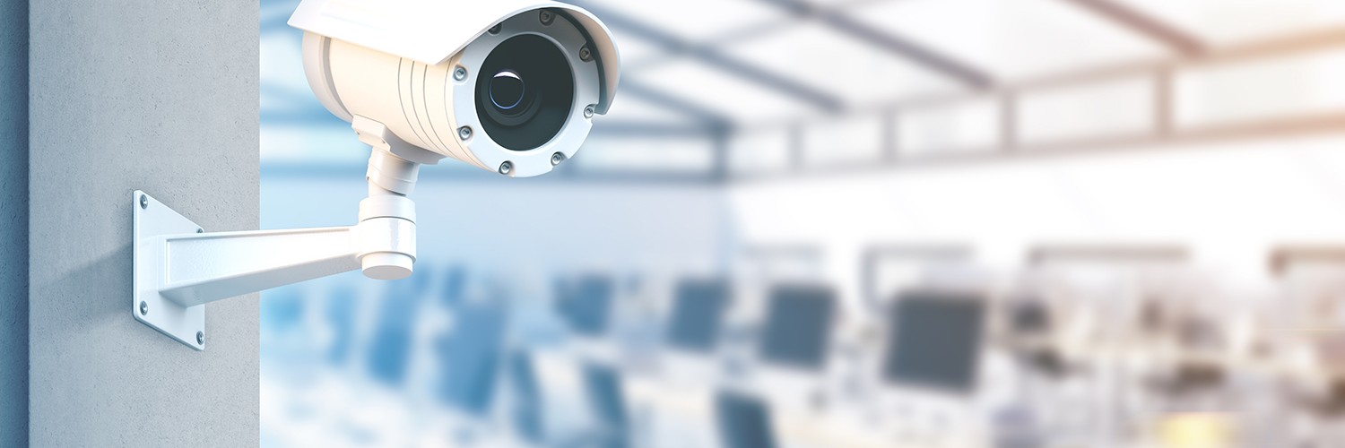 Beveiligingscamera in kantoorruimte met werkplekken, gericht op cameratoezicht op de werkvloer
